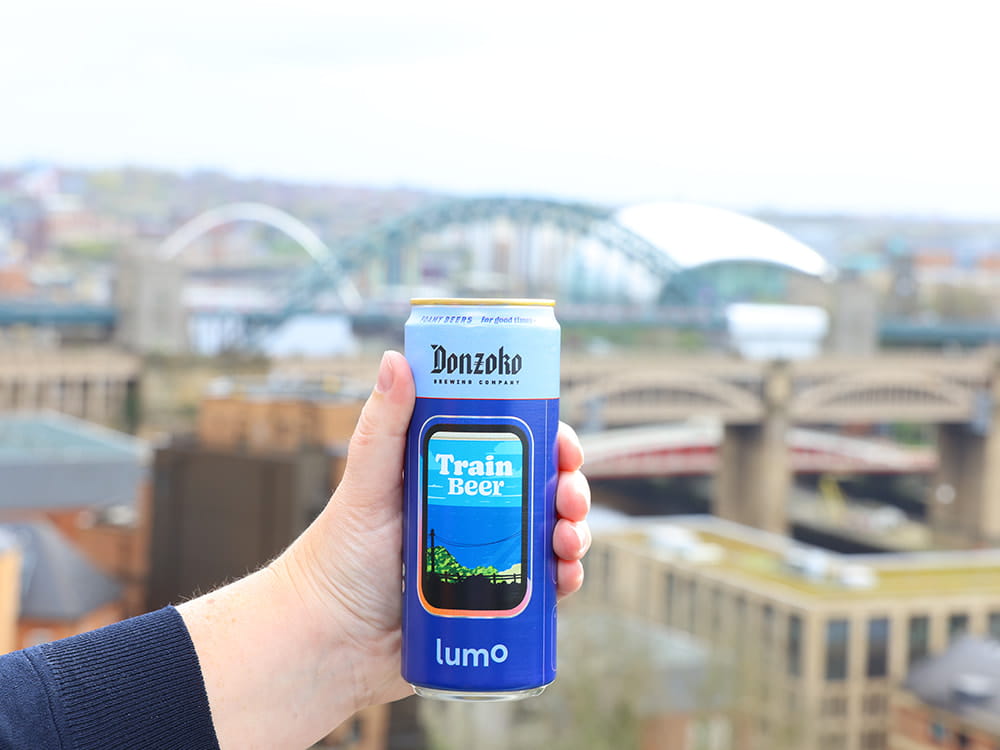 hand holding train beer can in front of Newcastle skyline