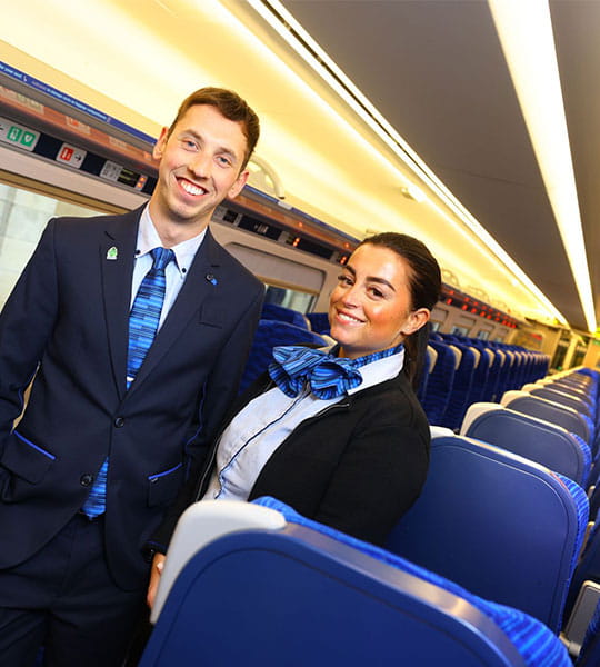 Two Lumo staff members in new uniforms standing on the aisle of the train